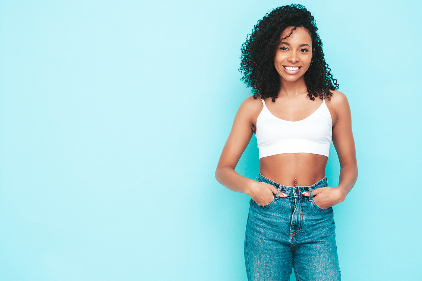 beautiful-black-woman-with-afro-curls-hairstyle-smiling-model-dressed-white-top-jeans-sexy-carefree-female-posing-near-blue-wall-studio-tanned-cheerful-isolated
