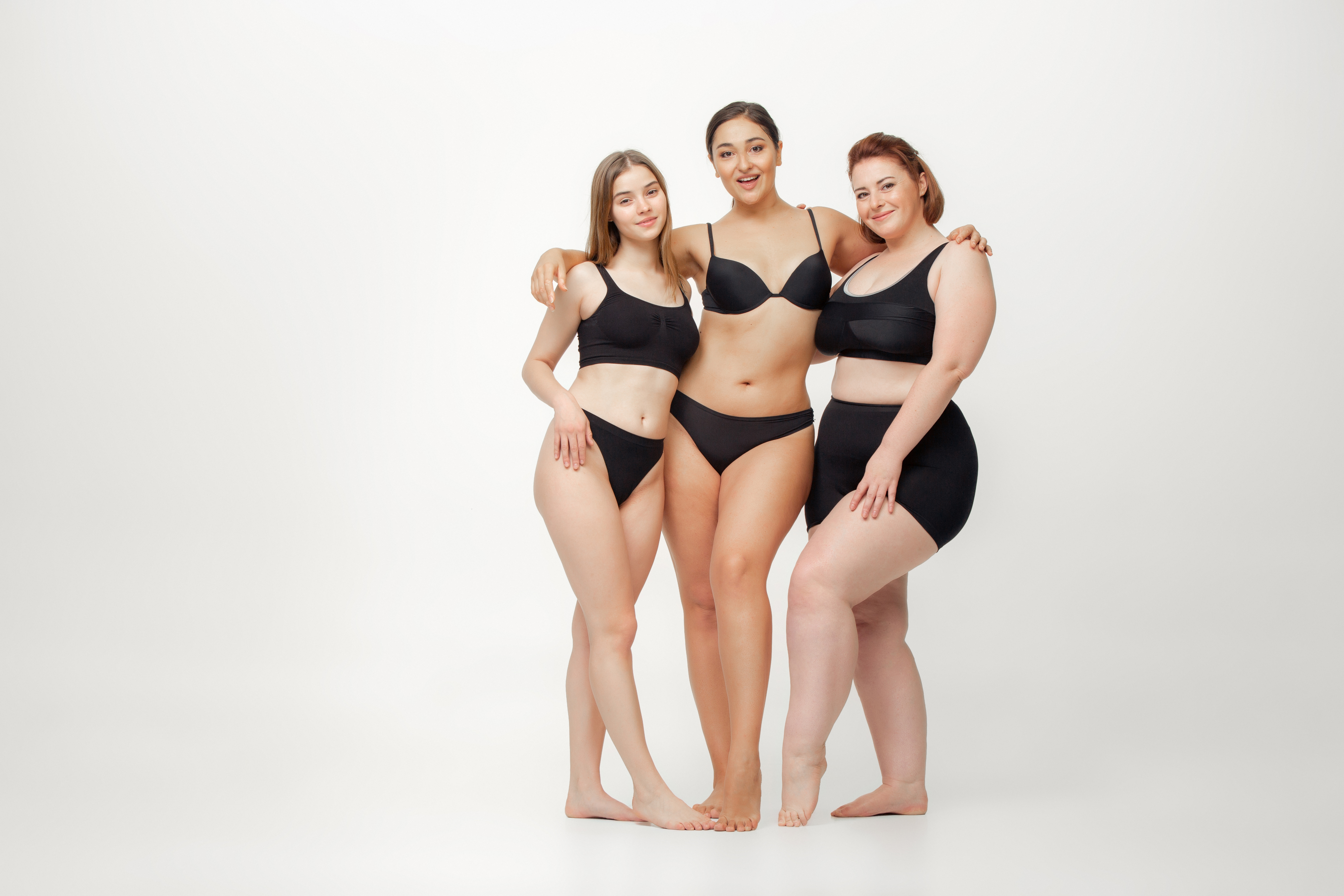 In love with myself. Portrait of beautiful young women with different shapes posing on white background. Happy female models. Concept of body positive, beauty, fashion, style, feminism. Diversity.